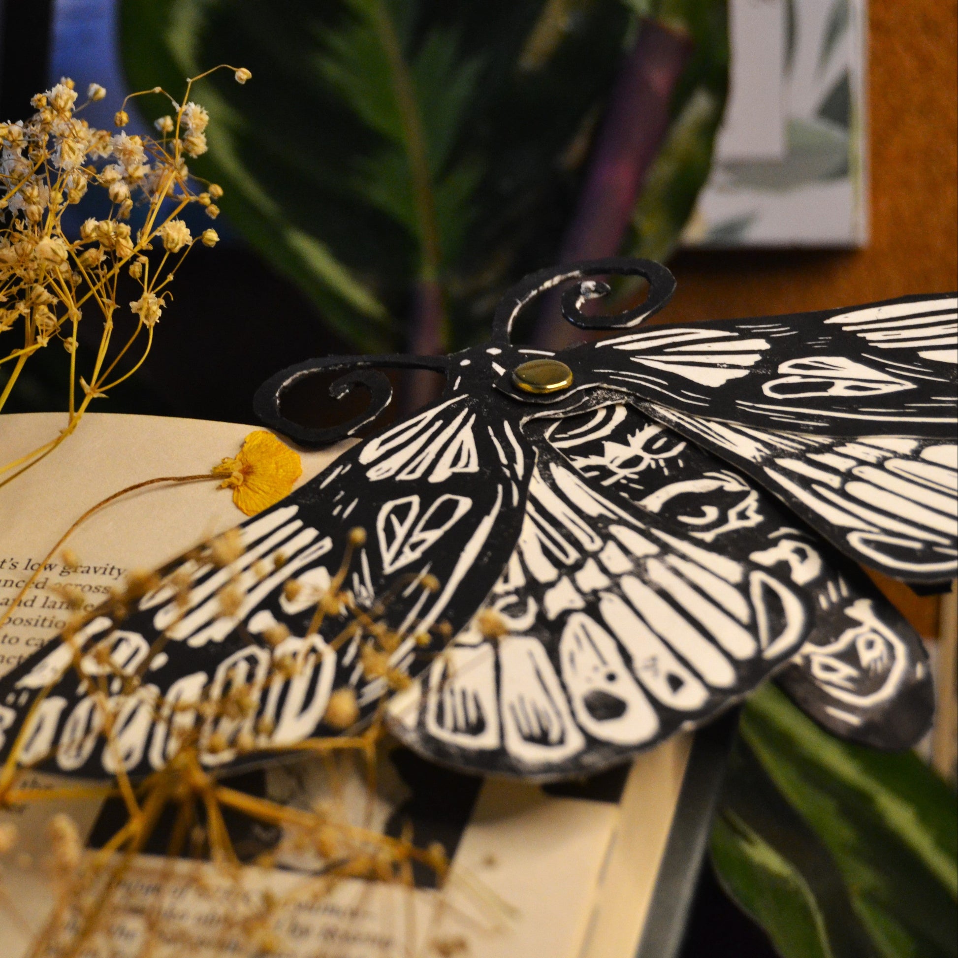 Moth-shaped book mark on an open book with dried flowers