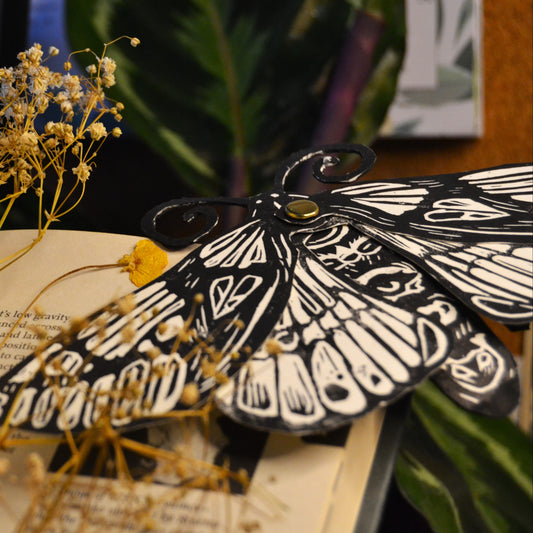 Moth-shaped book mark on an open book with dried flowers