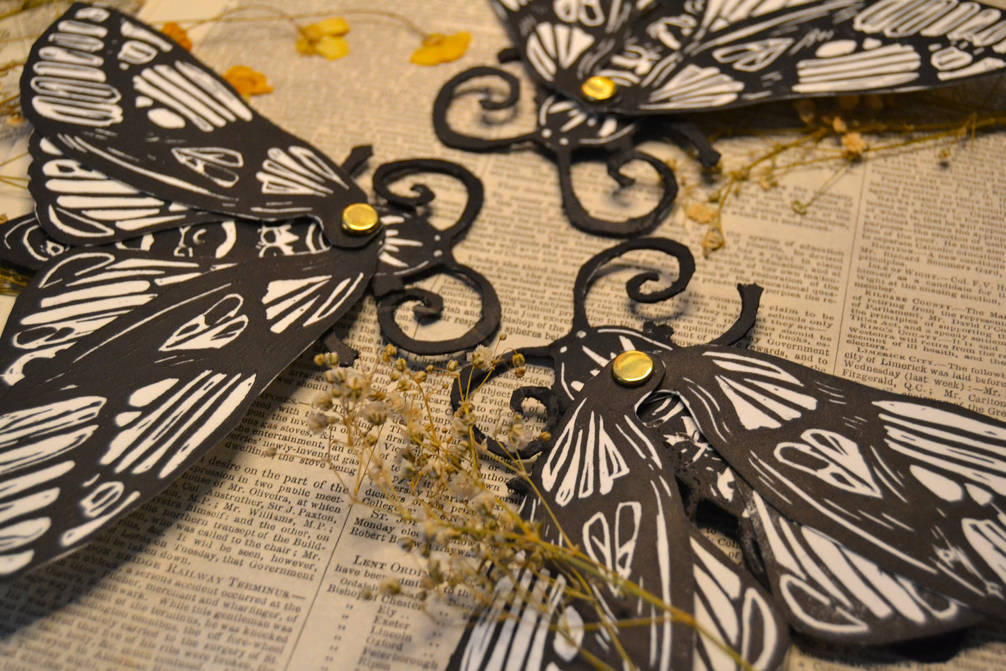 Black and white Moth-shaped bookmarks on a textured surface with dried flowers.