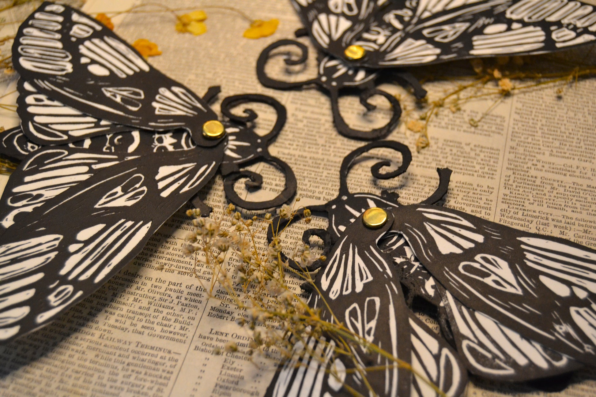 Black and white Moth-shaped bookmarks on a textured surface with dried flowers.