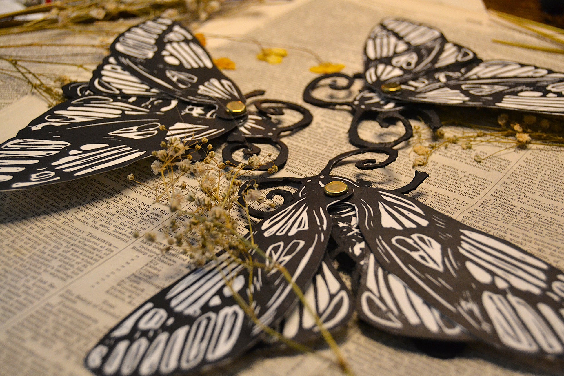 Black and white moth bookmarks on a textured surface with dried plants.