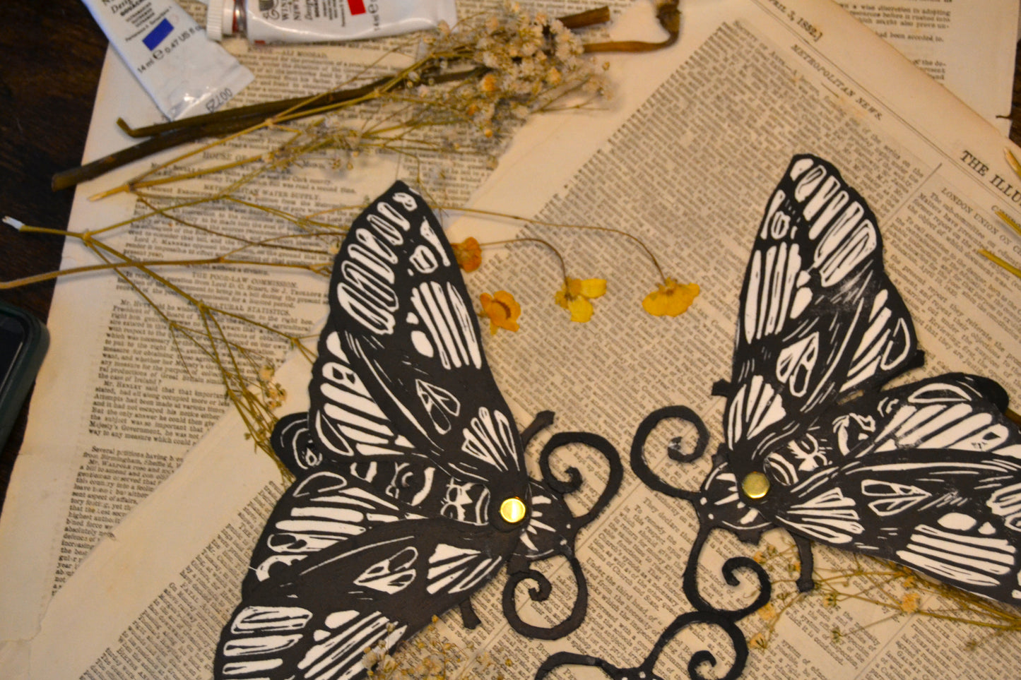 Two black and white moth bookmarks on a textured surface with flowers.